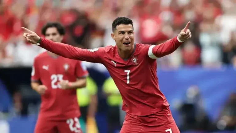 Balón de fútbol sobre el césped de un estadio con banderas de países participantes